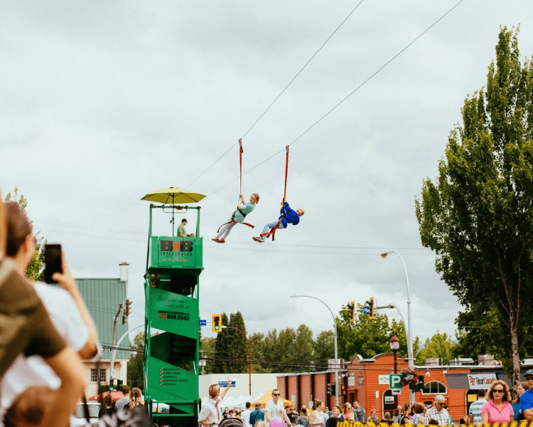 Two riders on the BC Event Makers zipline at an outdoor event